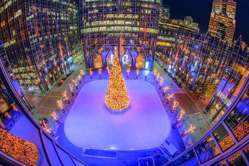 Aerial view of an outdoor rink lit in purple with a decorated Christmas tree at its center